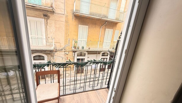 A balcony with a wooden chair, metal railing, and a view of a building with balconies and shutters. - MAX-FORTUNA (Ragusa)
