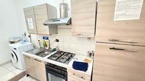 A compact kitchen with a gas stove, a washing machine, and wooden cabinets. - MAX-FORTUNA (Ragusa)