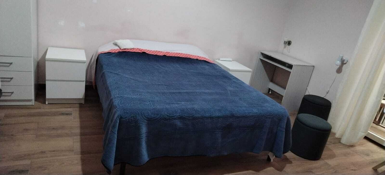 A bedroom with a bed, a nightstand, a dresser, and a trash bin.