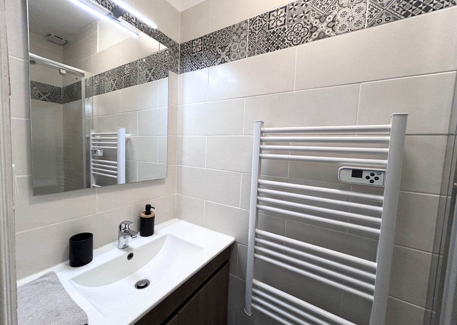 Une salle de bain avec un lavabo blanc, un miroir, un porte-serviettes et des carreaux décoratifs sur le mur.