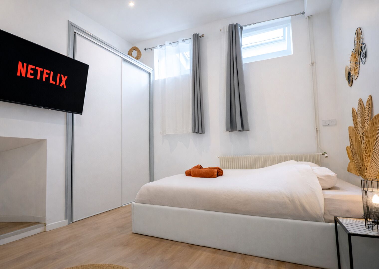 Un dormitorio moderno con cama, televisor montado en la pared, radiador y ventana con cortinas.
