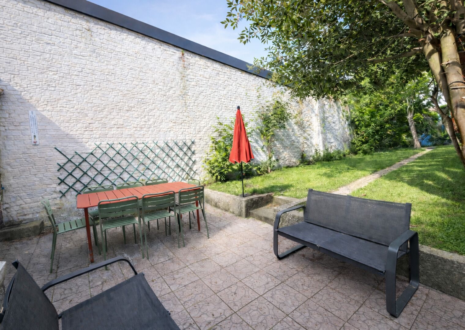 A patio area with a table and chairs, a bench, and a red umbrella.