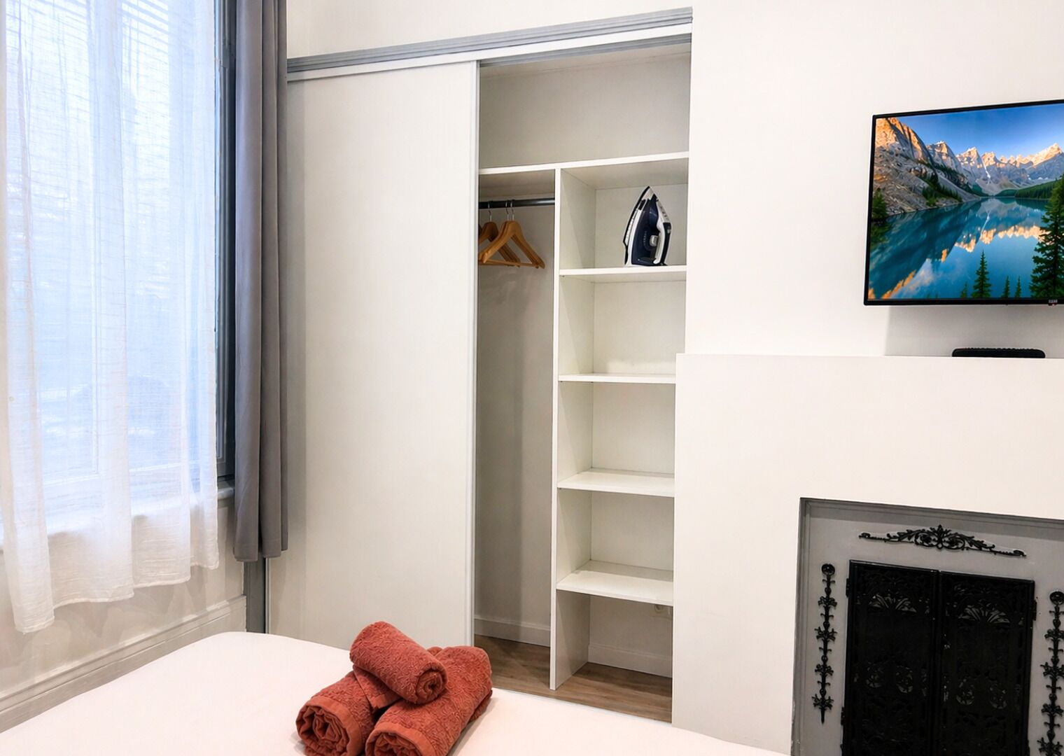 Ett hotellrum med en säng, en garderob med plats för att hänga kläder, en tv som är monterad på väggen och en öppen spis.