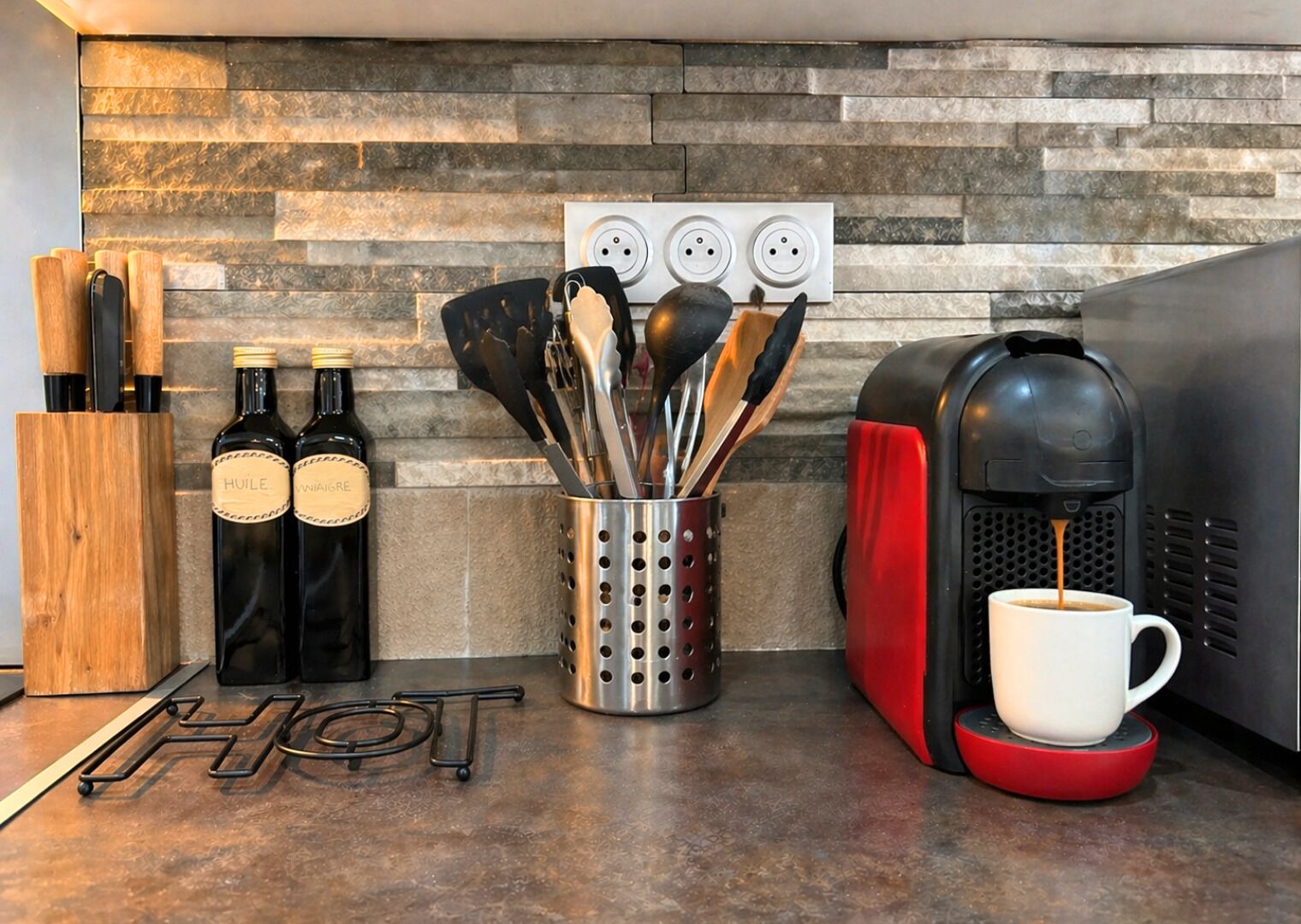 Une cuisine équipée d’une machine à café, de deux bouteilles de vin, d’un bloc à couteaux et d’un porte-ustensiles.