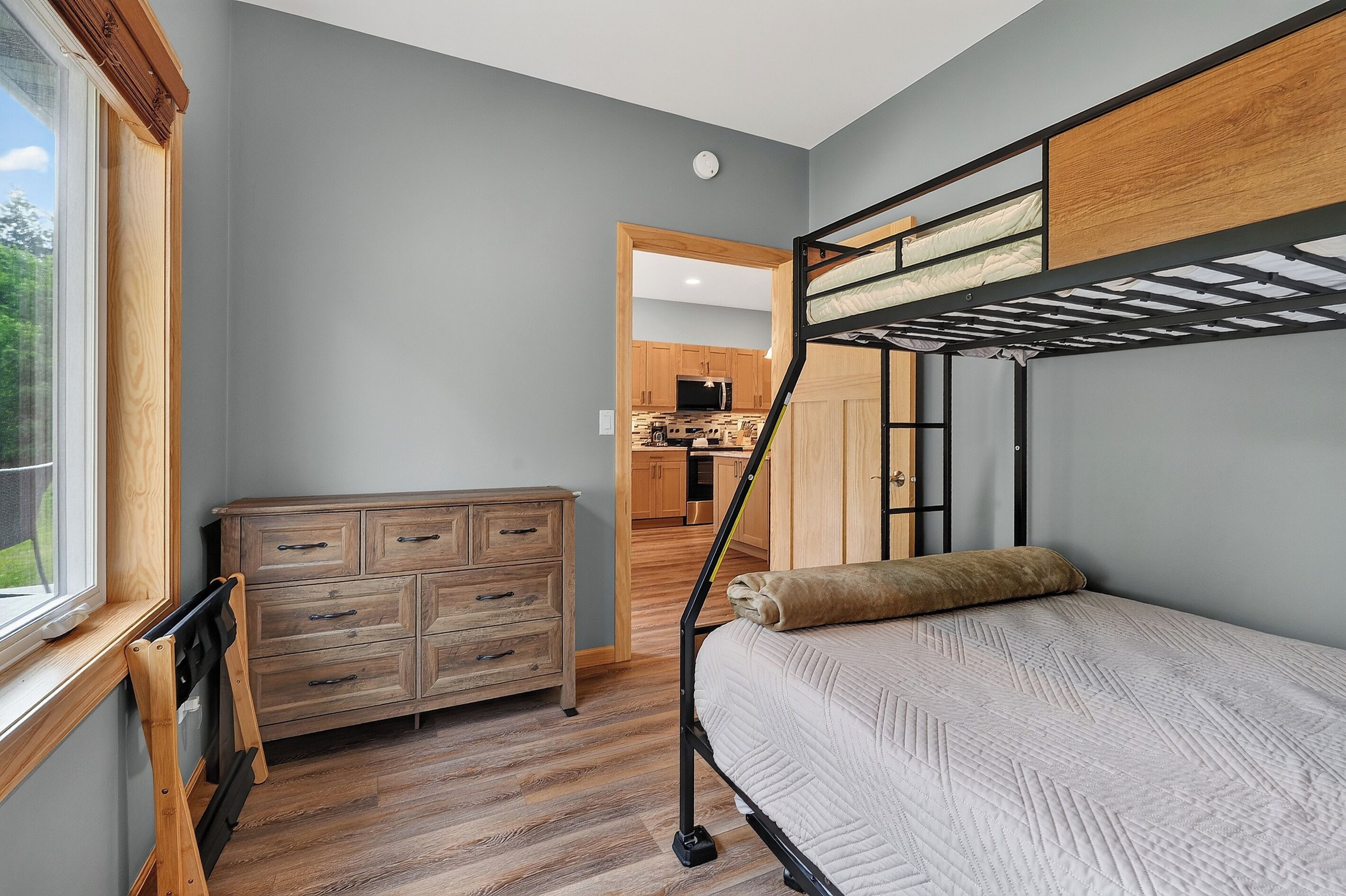 Ein Stockbett mit Kopfstütze, eine Holzkommode und ein Fenster mit Jalousien.