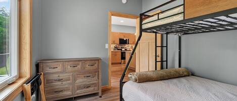 Ein Stockbett mit Kopfstütze, eine Holzkommode und ein Fenster mit Jalousien.