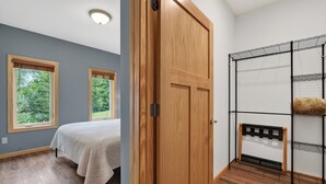 A bedroom with a bed, two windows, a wooden door, and a metal shelving unit.