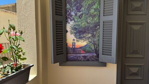 A balcony with a cushioned seating area, a potted plant, and a wall-mounted picture of a sunset scene. - Bayt Al Yasmin - Ehden (Ehden)