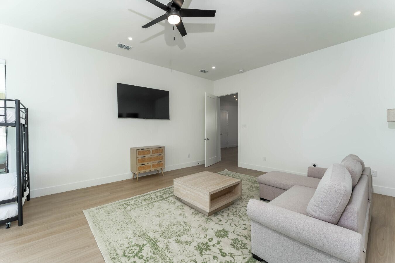 Un salon moderne doté d’un téléviseur à écran plat, d’un ventilateur de plafond, d’une table basse en bois, d’un canapé beige et d’un tapis de couleur claire.