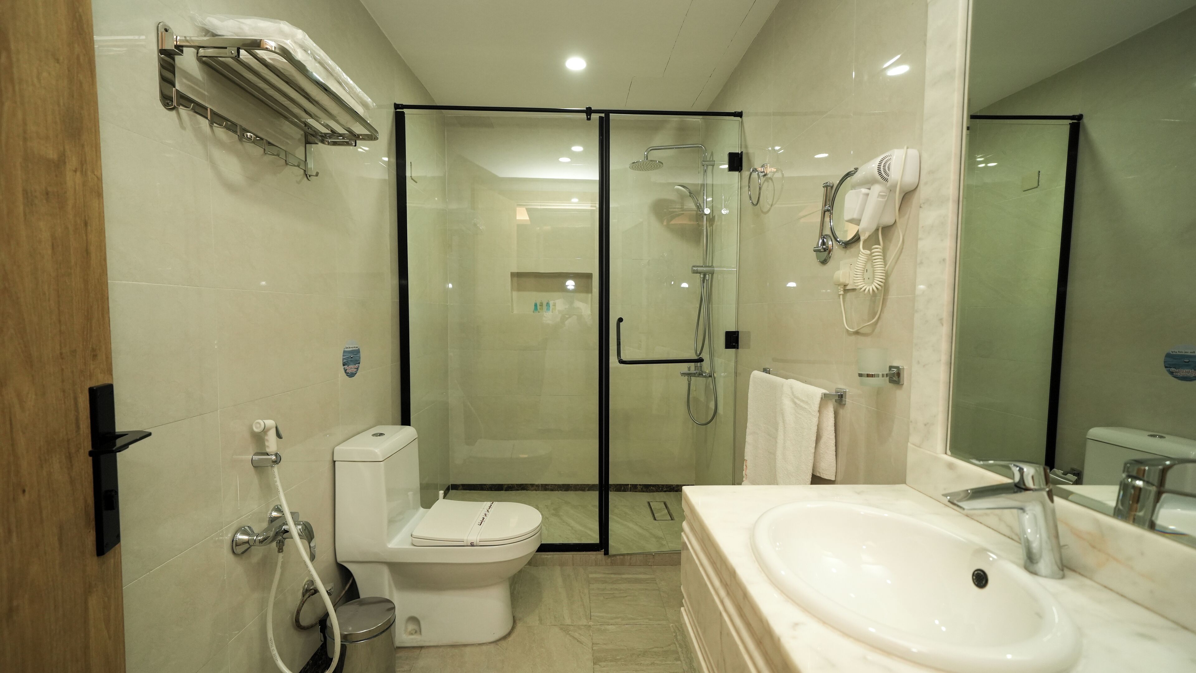 A modern bathroom with a glass-enclosed shower, a toilet, a sink, and a hairdryer mounted on the wall.