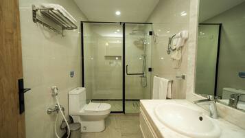 A modern bathroom with a glass-enclosed shower, a toilet, a sink, and a hairdryer mounted on the wall.