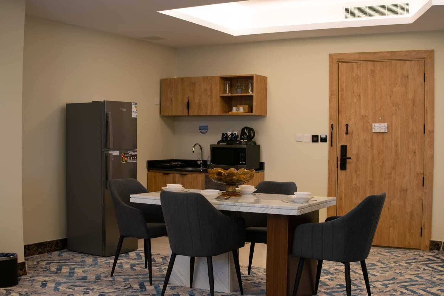 A compact kitchen with a refrigerator, microwave, and wooden cabinets. There is a dining table with four chairs and a decorative centerpiece.
