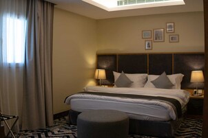 Habitación de hotel con una cama grande, dos lámparas de noche, un cabecero decorado con arte y una ventana con cortinas.