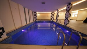 An indoor swimming pool with clear blue water, tiled walls, and a modern design. - benzrthotel (Al-Hofuf)
