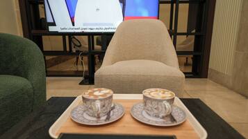 A room with a green chair, a beige chair, and a tray with two cups of coffee.
