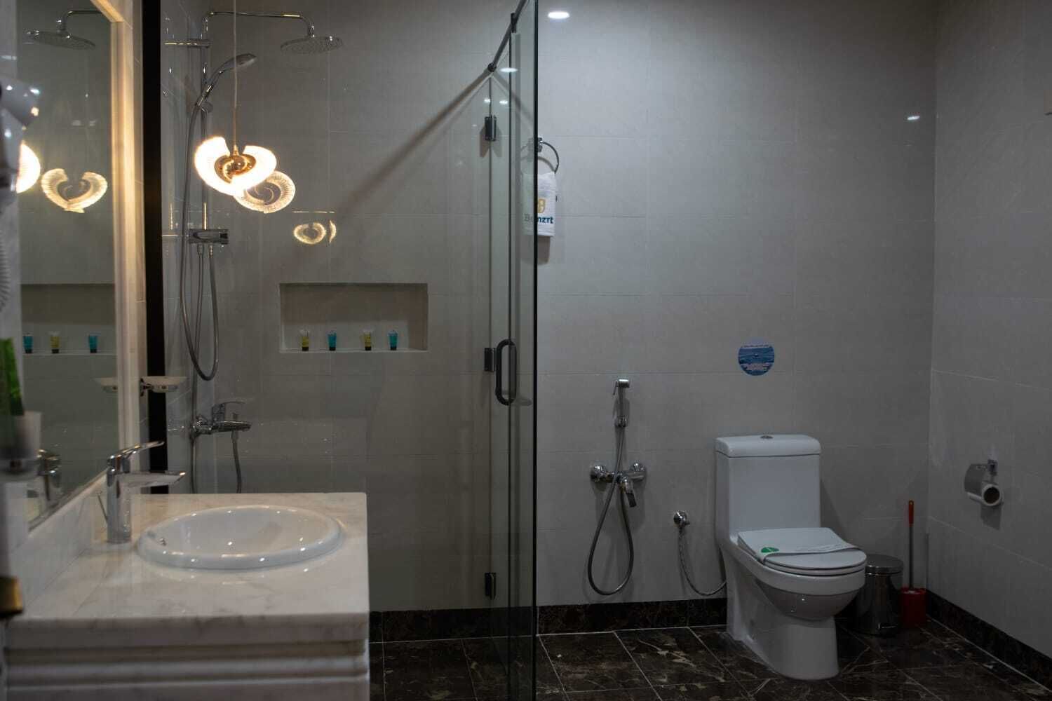 Un baño moderno con ducha envuelta en vidrio, inodoro blanco y lavamanos de mármol.