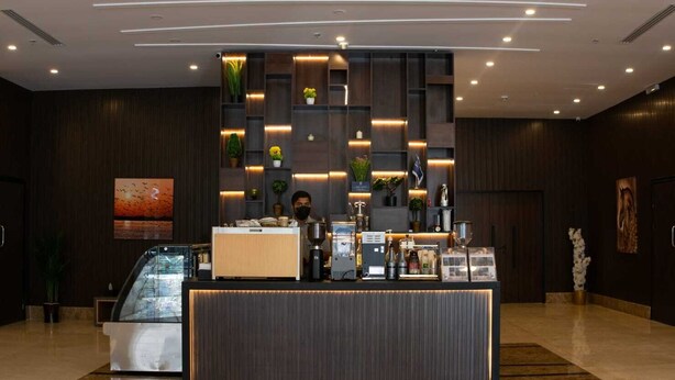 A reception desk with a coffee machine, a glass display case, and a plant. - benzrthotel (Al-Hofuf)
