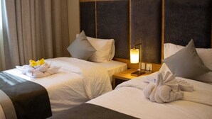 A hotel room with two beds, each with white linens and pillows, a bedside table with a lamp, and a window with curtains. - benzrthotel (Al-Hofuf)