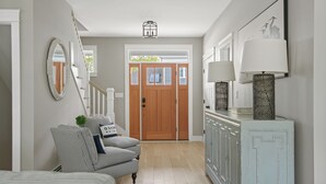 A hallway with a wooden door, a striped armchair, a cabinet with a lamp, and a mirror on the wall. - Downtown Coastal Charm Cottage in Kennebunk (Kennebunk)