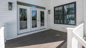A covered porch with a white railing, a sliding glass door, and a large window. - Downtown Coastal Charm Cottage in Kennebunk (Kennebunk)