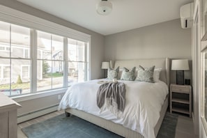 A bedroom with a large window, a bed with pillows, a bedside table with a lamp, and a heater. - Downtown Coastal Charm Cottage in Kennebunk (Kennebunk)