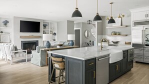 A modern kitchen with a central island, bar stools, a flat-screen TV, and a fireplace. - Downtown Coastal Charm Cottage in Kennebunk (Kennebunk)