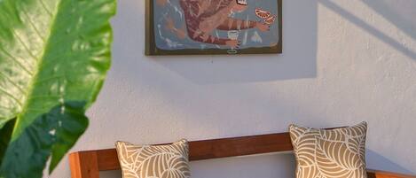 A wooden bench with patterned cushions, a wall-mounted abstract painting, and a large green plant in the foreground.