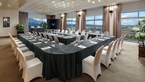 A conference room with a panoramic city view, equipped with a large table, chairs, and a television screen. - INEZA HOTEL (Ruhengeri)