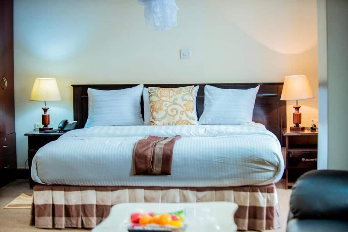 A neatly made bed with a striped bedspread, two bedside lamps, and a fruit bowl on the nightstand.
