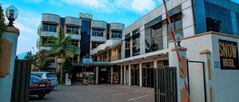 Un hotel de diseño moderno, con un letrero visible, entrada protegida por un portón y zona de estacionamiento.