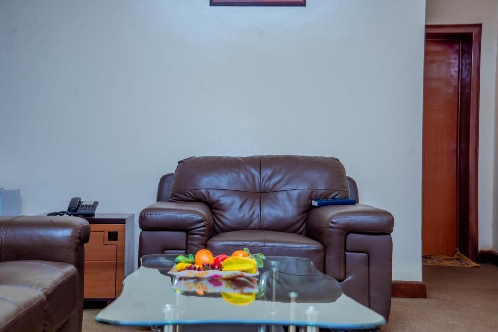 A living room with a brown leather sofa, a glass coffee table with fruit, and a wooden side table with a phone.