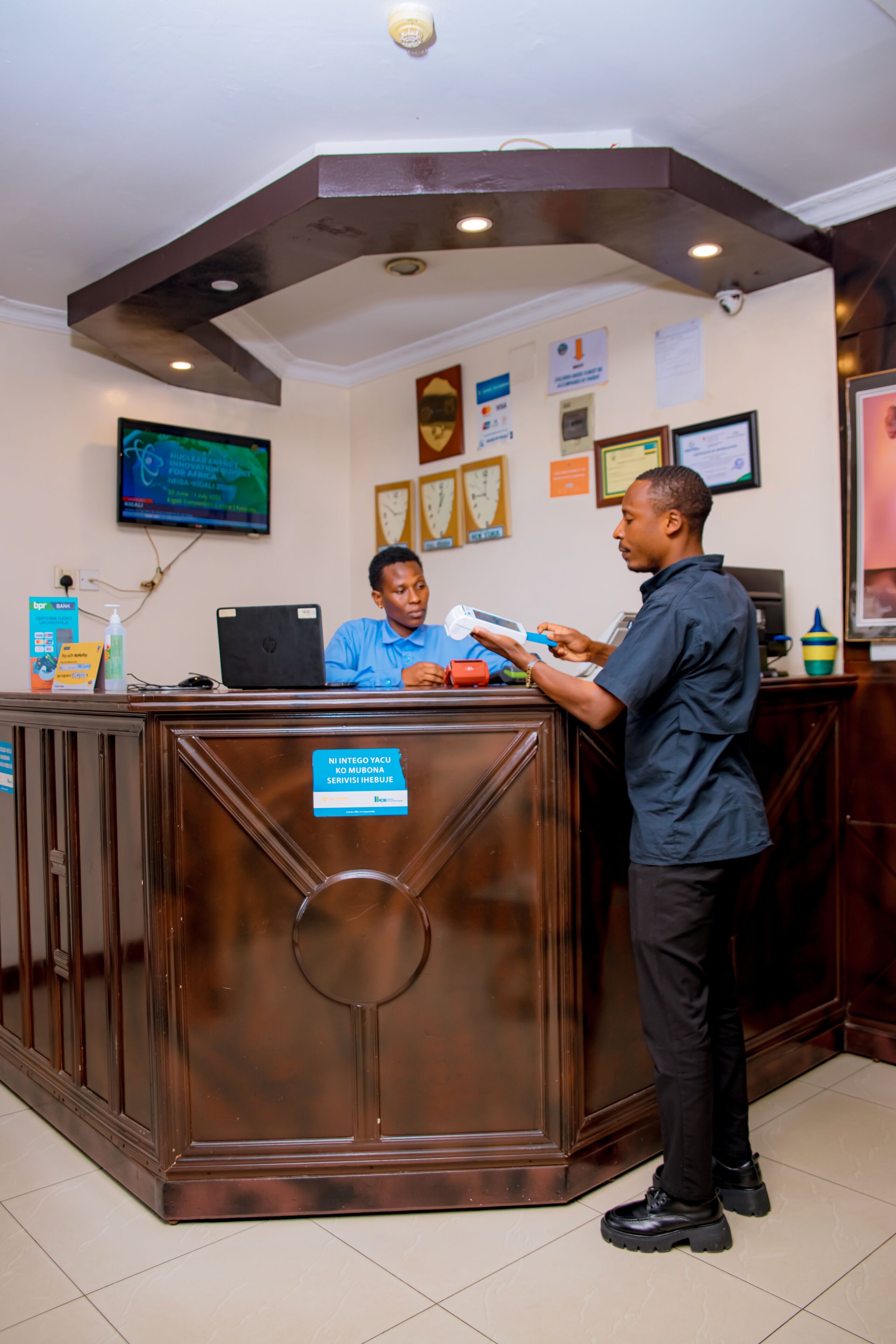 A reception desk with a digital screen, a laptop, and a sign indicating a service area.