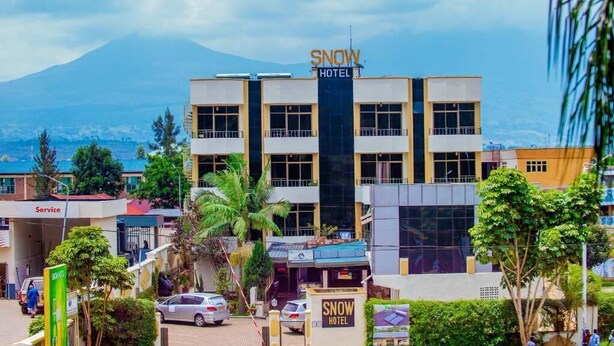 A hotel named 'SNOW HOTEL' with a prominent sign, surrounded by greenery and a view of a mountain in the background. - INEZA HOTEL (Ruhengeri)
