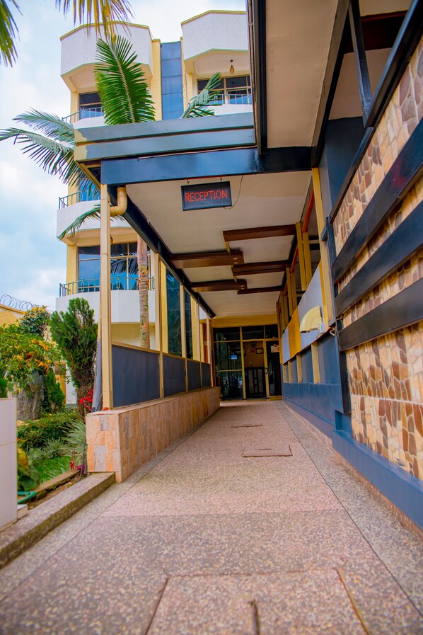 A reception area with a sign indicating it's the reception, a tiled floor, and a view of the building's exterior. - INEZA HOTEL (Ruhengeri)