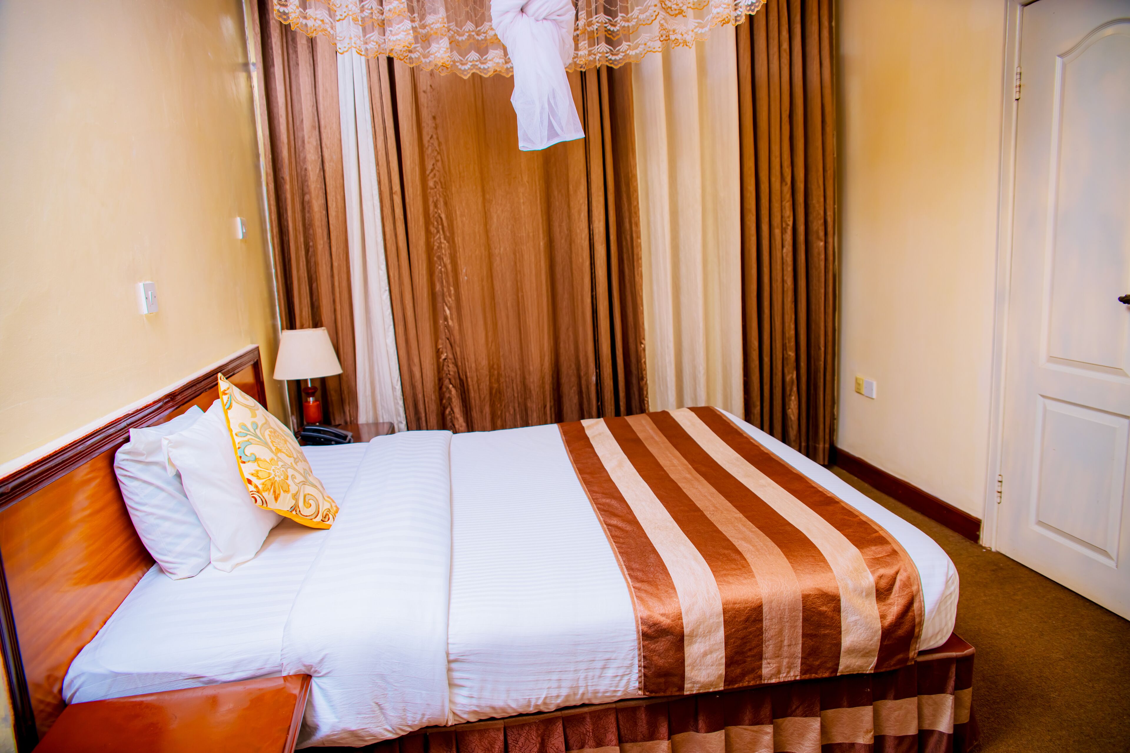 Una cama bien tendida con una colcha a rayas, un cabecero de madera y una única almohada decorativa.