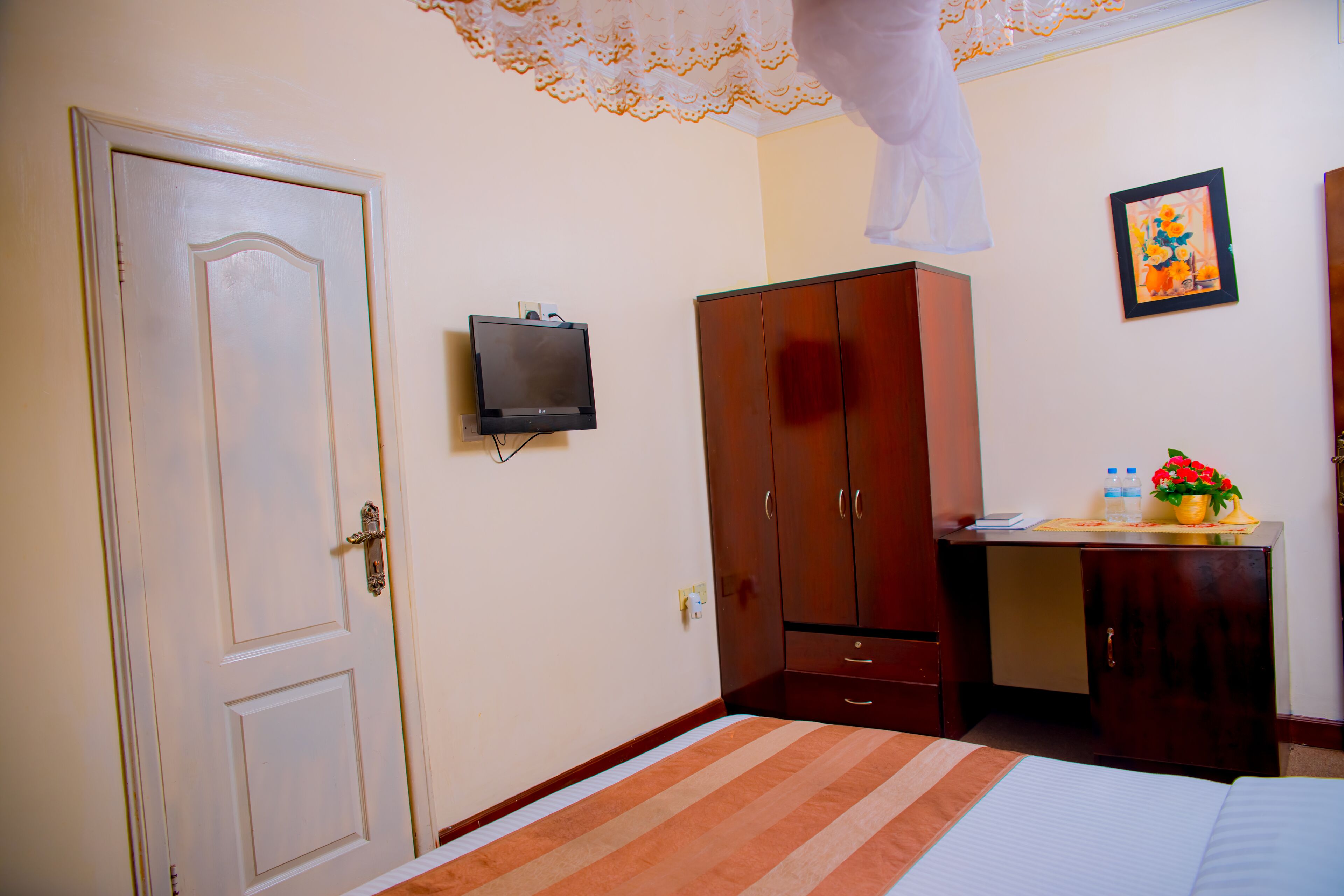 Una habitación de hotel con cama, armario, escritorio con silla, televisión y un cuadro en la pared.
