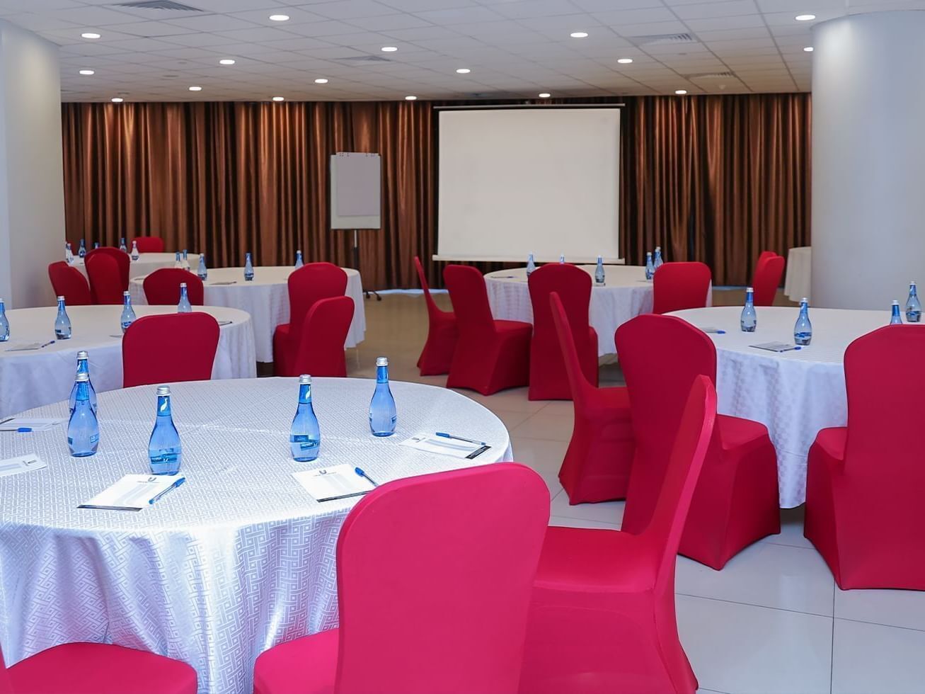 A conference room with round tables, red chairs, and water bottles.
