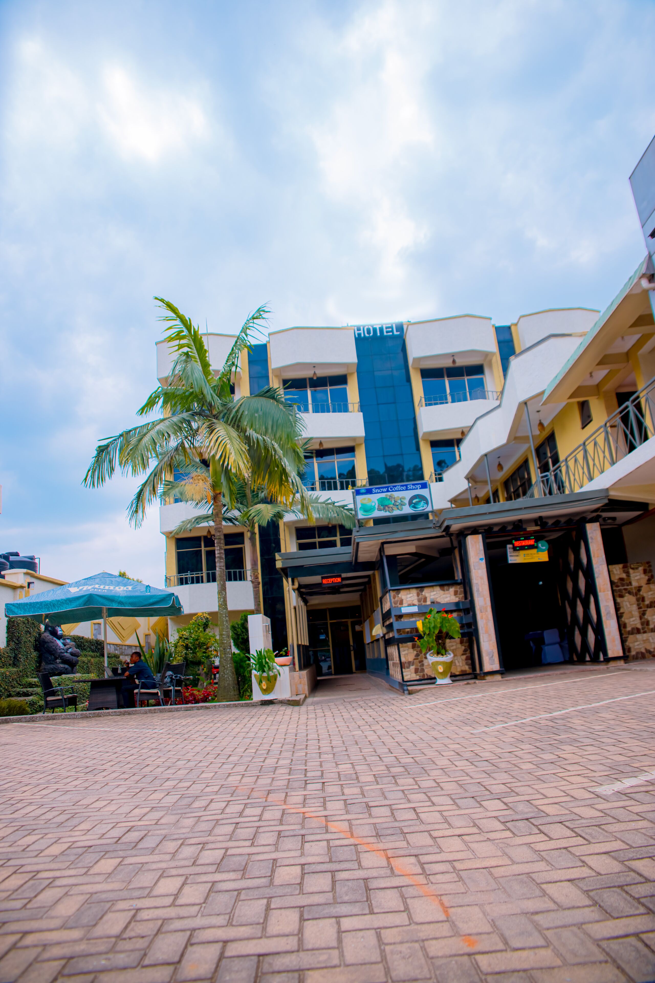 A hotel with a modern design, featuring a central entrance, a coffee shop, and a palm tree.