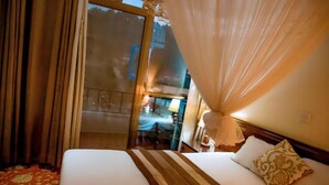 A hotel room with a bed, a window with curtains, a bedside table with a lamp, and a view of the outside. - INEZA HOTEL (Ruhengeri)