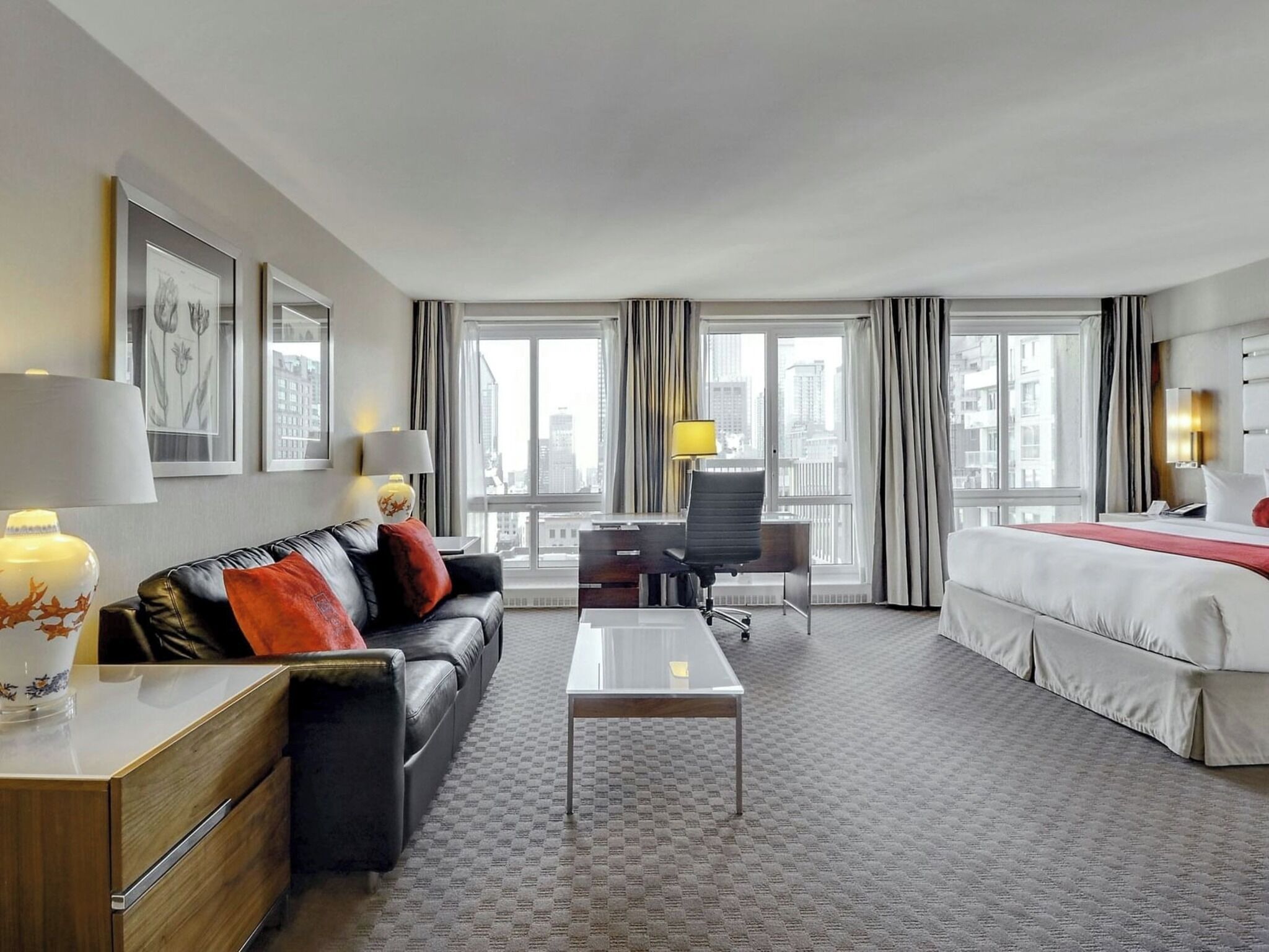Een hotelkamer met een bed, een bureau, een bank en uitzicht op de stad.
