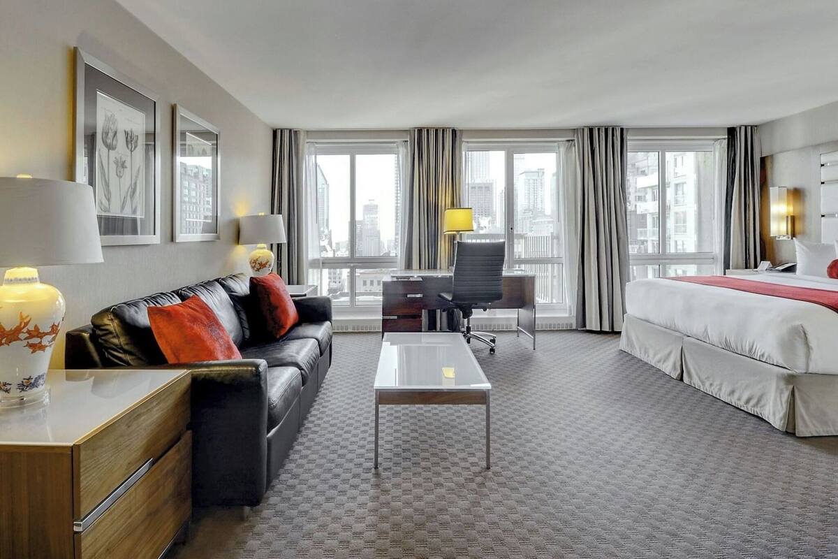 A hotel room with a bed, a desk, a sofa, and a view of the city.
