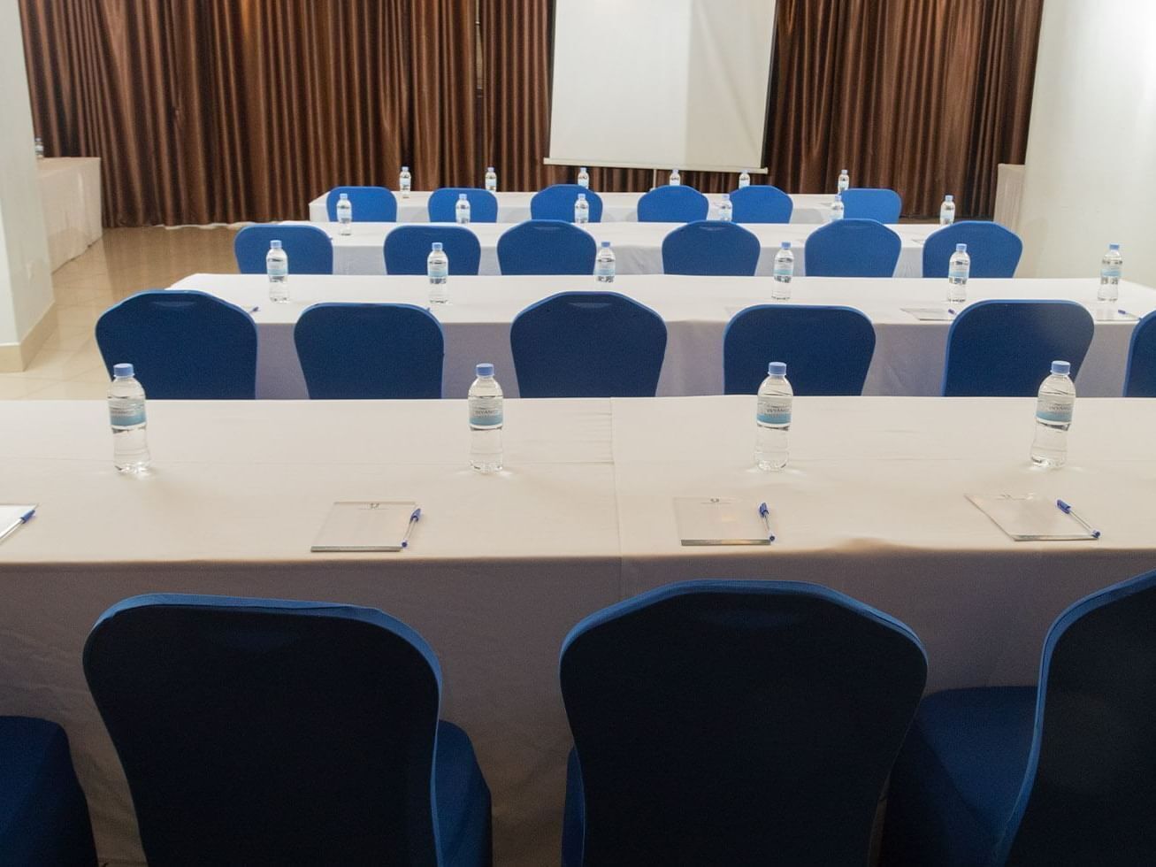 Un salón de conferencias con mesas largas, sillas azules, botellas de agua y tarjetas de identificación.