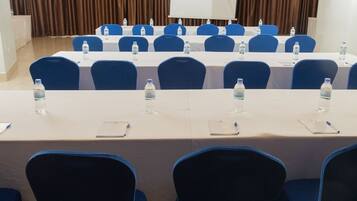 Un salón de conferencias con mesas largas, sillas azules, botellas de agua y tarjetas de identificación.