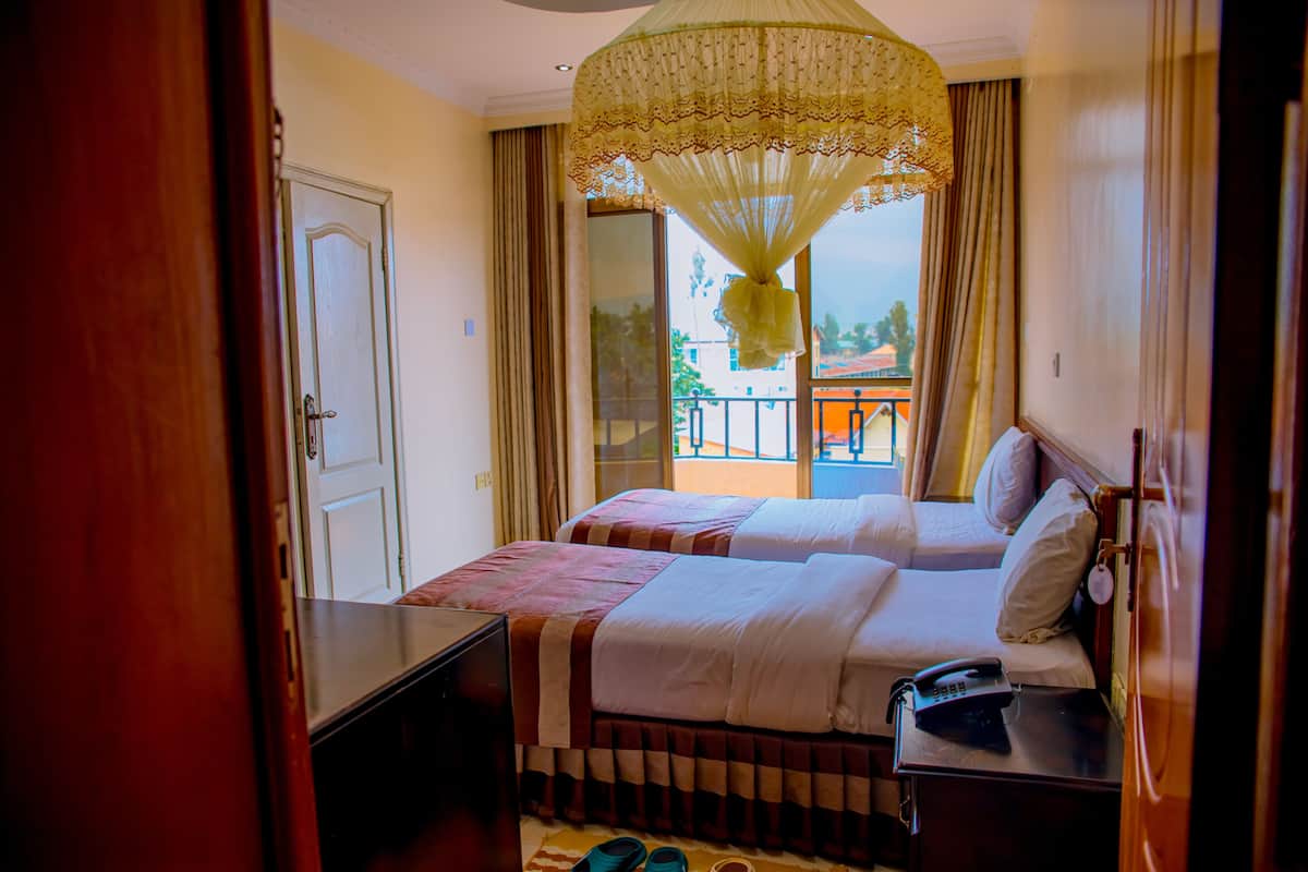 A hotel room with two beds, a desk, a telephone, and a balcony with a view.