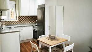 A compact kitchen with white cabinets, a wooden dining table with four chairs, and a refrigerator.