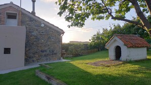 A stone building with a small attached structure, a grassy yard, and a wooden fence.