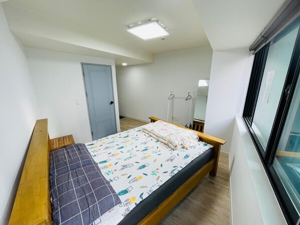 A bedroom with a bed, a window, a door, and a ceiling light.