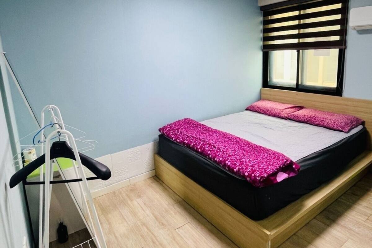 A bedroom with a bed, a window with blinds, a ceiling light, and a wall-mounted air conditioner.
