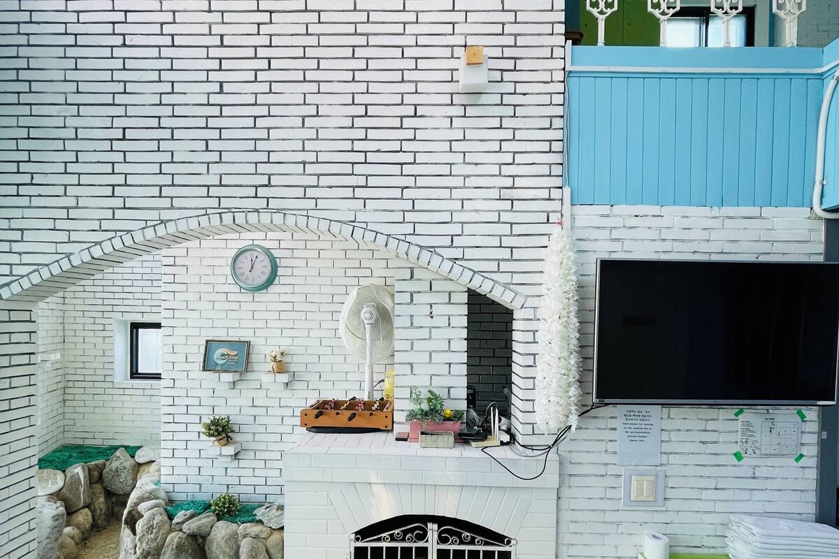 A room with a white brick wall, a fireplace, a green cabinet, and a blue upper level with decorative elements.