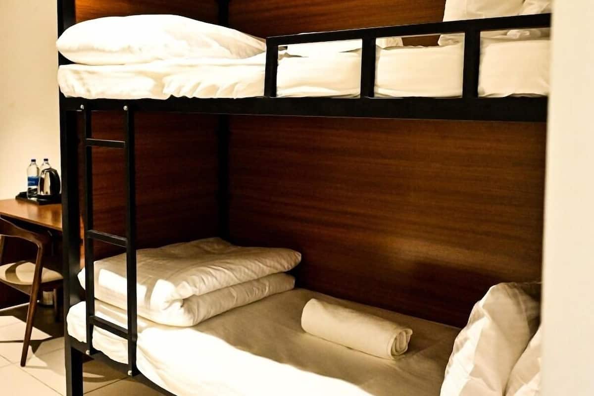 A bunk bed with two levels, each with pillows and a blanket. A desk with a chair and a water bottle is visible to the left.